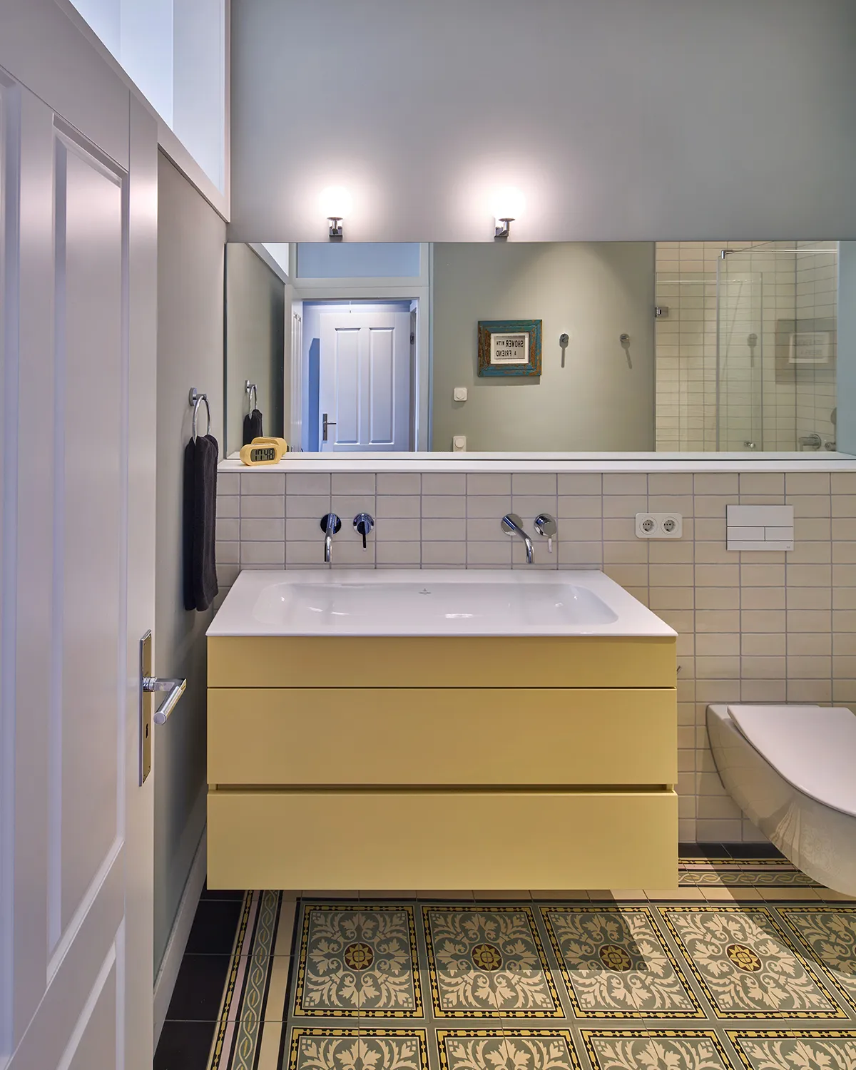 Badezimmer im Umbau einer Maisonettewohnung mit gelbem Waschtisch, großem Spiegel und ornamentalen Jugendstilfliesen.